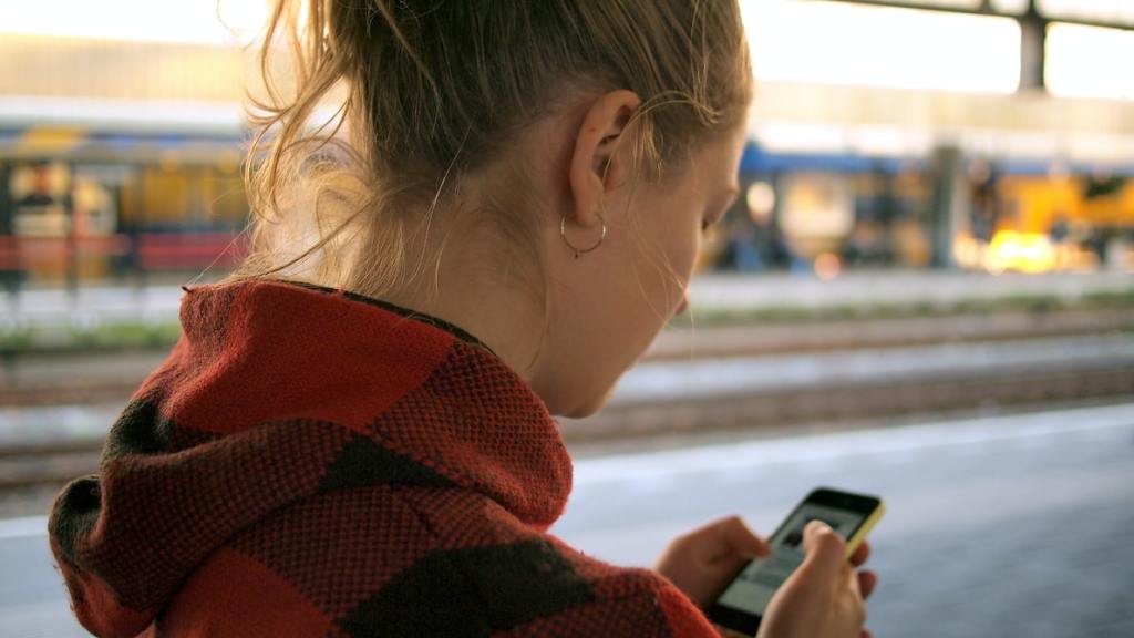 VIVE app image. A woman at a train station looking at her phone